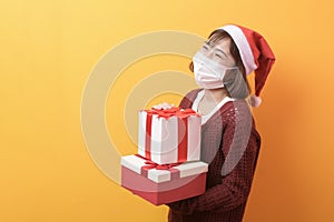 Portrait of young smiling woman in surgical mask wearing red Santa Claus hat isolated yellow  background studio