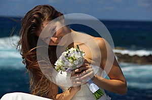 Portrait of young smilling bride in white wedding dress with flowers in hand. Wedding ceremony on ocean coast