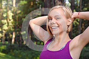 Portrait of young smilling sporty woman stretching in the fores outdoor early in the morning