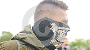 Portrait of young soldier in military uniform with cloth mask on his face. Sports game using a copy of a firearm. Close