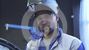 Portrait of young specialist auto mechanic in welding helmet on the background of modern car service. Slow motion