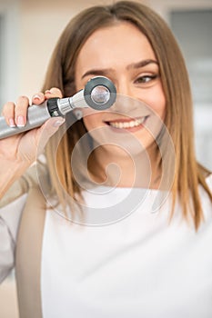 Portrait of young specialist dermatologist with dermatoscope in uniform and gloves in doctor office before examination