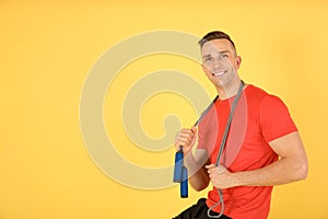 Portrait of young sportive man with jump rope on color background.