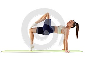 Portrait of young sportive woman training, doing stretching exercises isolated over white background. Strong body