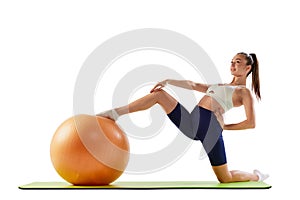 Portrait of young sportive woman training, doing stretching exercises with rubber fitness ball isolated over white