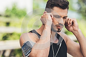 portrait of young sportsman in earphones with smartphone in running armband