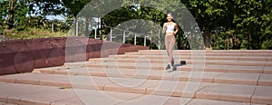 Portrait of young sportswoman running on street. Fitness girl jogging in park, workout outdoors, listening music in