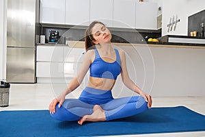 Portrait of young sportswoman, stretching her neck, warm-up before yoga exercises, doing fitness workout on rubber mat