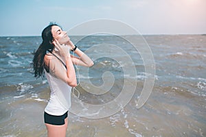 Portrait of young sporty woman in headphones relaxing while sitting near ocean in summer , attractive female listening