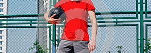 Portrait of a young strong basketball player holding a black basketball and wearing a red t-shirt