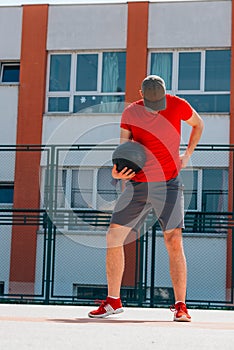 Portrait of a young strong basketball player holding a black basketball and wearing a red t-shirt