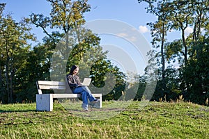 Portrait of young student, girl using laptop, sitting in park on bench, typing on computer