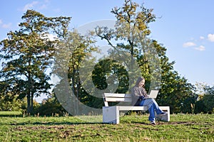 Portrait of young student, girl using laptop, sitting in park on bench, typing on computer