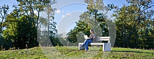 Portrait of young student, girl using laptop, sitting in park on bench, typing on computer