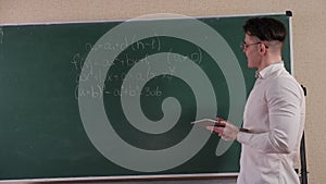 Portrait of a young student in glasses with a tablet near the blackboard.