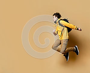 Portrait of a young student man jumping in the studio on a beige background