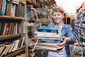 Portrait of a young student offering a book.man with lots of books in his hands is in the library and smiles