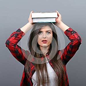 Portrait of a young student woman holding books on head against gray background.Tired of learning/studying concept