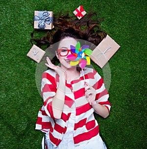 Portrait of a young styled redhead woman with pinwheel toy present around lying down on green spring grass, above point of view