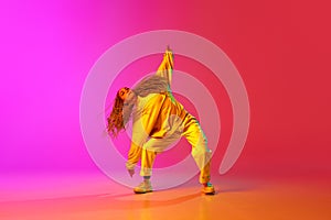 Portrait of young stylish girl, hip-hop dancer training in casual clothes over gradient pink background in neon light