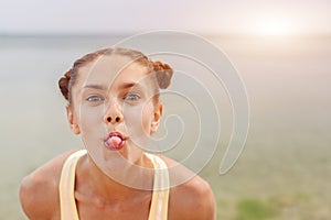 Portrait of young stylish laughing girl model summer natural makeup outside on the beach. Looking at camera showing her tongue