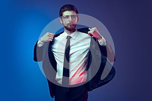 Portrait of young stylish man in business suit posing isolated on dark blue studio background. Concept of human emotions