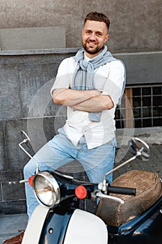 Portrait of a young and stylish man with a moped in summer sunny day in european city