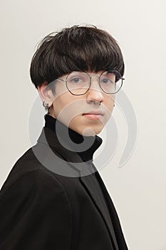 Portrait of young stylish man with piercing, in glasses posing, looking at camera  over grey studio background