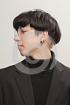 Portrait of young stylish man with piercing, in glasses posing  over grey studio background