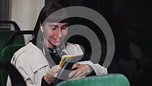 Portrait of young stylish woman in headphones listening to music and browsing on mobile phone in public transport. Young