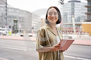 Portrait of young stylish woman walking with tablet, going somewhere in city