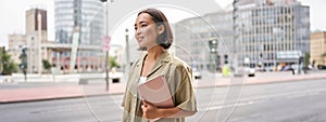 Portrait of young stylish woman walking with tablet, going somewhere in city