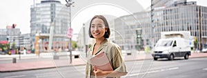 Portrait of young stylish woman walking with tablet, going somewhere in city