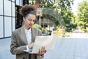 Portrait of young successful businesswoman office worker using laptop computer outside office building in formal wear.