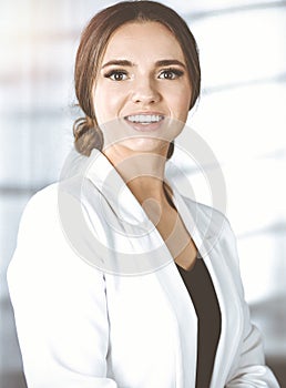 Portrait of young successful businesswoman, while she is standing near the desk in a sunny modern office. Business