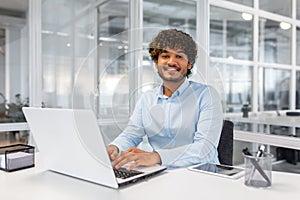 Portrait of young successful contemporary businessman inside office, man at workplace smiling and looking at camera