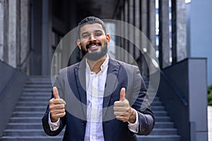Portrait of young successful Muslim man businessman, lawyer standing near court building in suit, smiling and pointing