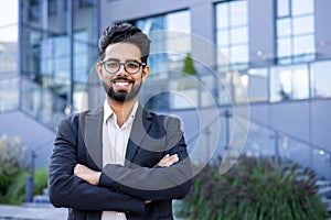 Portrait of a young successful and smiling Muslim male businessman standing outside an office building in a suit and