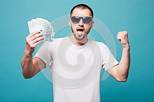 Portrait of a young summer man on white t-shirt holding cash money victory scream while smiling isolated on green background