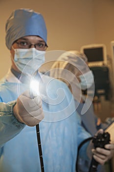 Portrait of young surgeon holding a medical instrument towards the camera, light shining