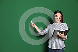 Portrait of young teacher with book and chalk on green background