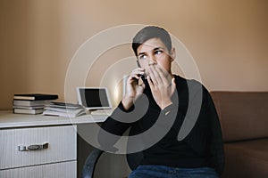 Portrait of young teenage boy at home speaking by phone and surprised. Background of tablet and books