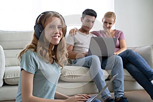 Portrait of young teenage daughter sit on the floor using laptop to studying online and looking at camera while parents sit on