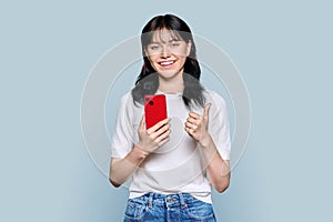 Portrait of young teenage female with mobile phone showing ok gesture
