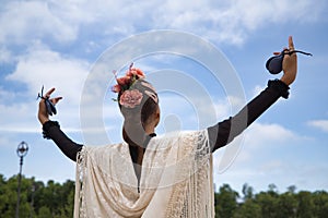 Portrait of young teenage girl in black dance dress, white shawl and pink carnations in her hair, dancing flamenco with castanets