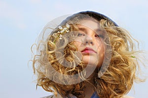 Portrait of young teenage girl with curly hair wearing a hood, blue sky background. People, travel, teens concept.