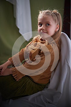 Portrait of a young teenage girl sitting on chair among a green and white fabric background in a photo studio. A little