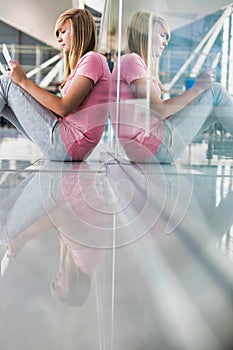 Portrait of young teenage girl sitting on the floor and using digital tablet while waiting for her flight in airport