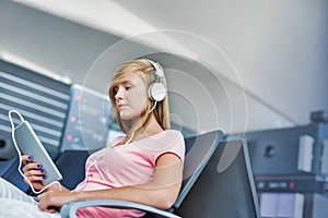 Portrait of young teenage girl sitting while watching movie on her digital tablet with headphones on in airport