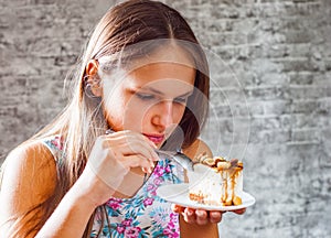 Young teenager brunette girl with long hair eating cake dessert on gray wall background